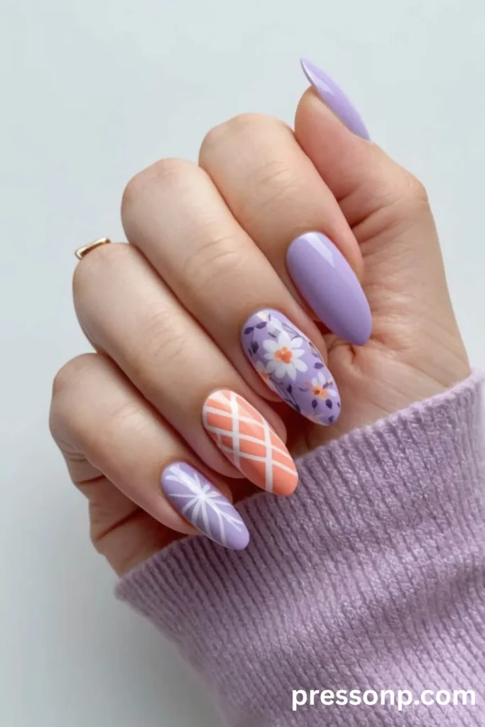 Close-up of a hand with almond-shaped manicure featuring coral and lavender nail art, paired with a matching lavender knit sweater sleeve.