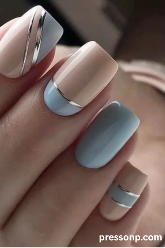 Close-up of square-shaped nails with a pastel blue and nude geometric design, separated by metallic silver striping lines.
