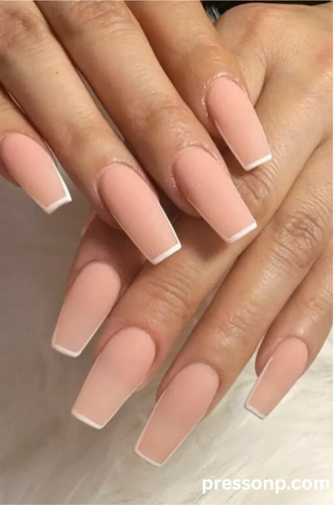 Close-up of hands with long coffin-shaped nails featuring a smooth matte  base and clean, thin white French tips.