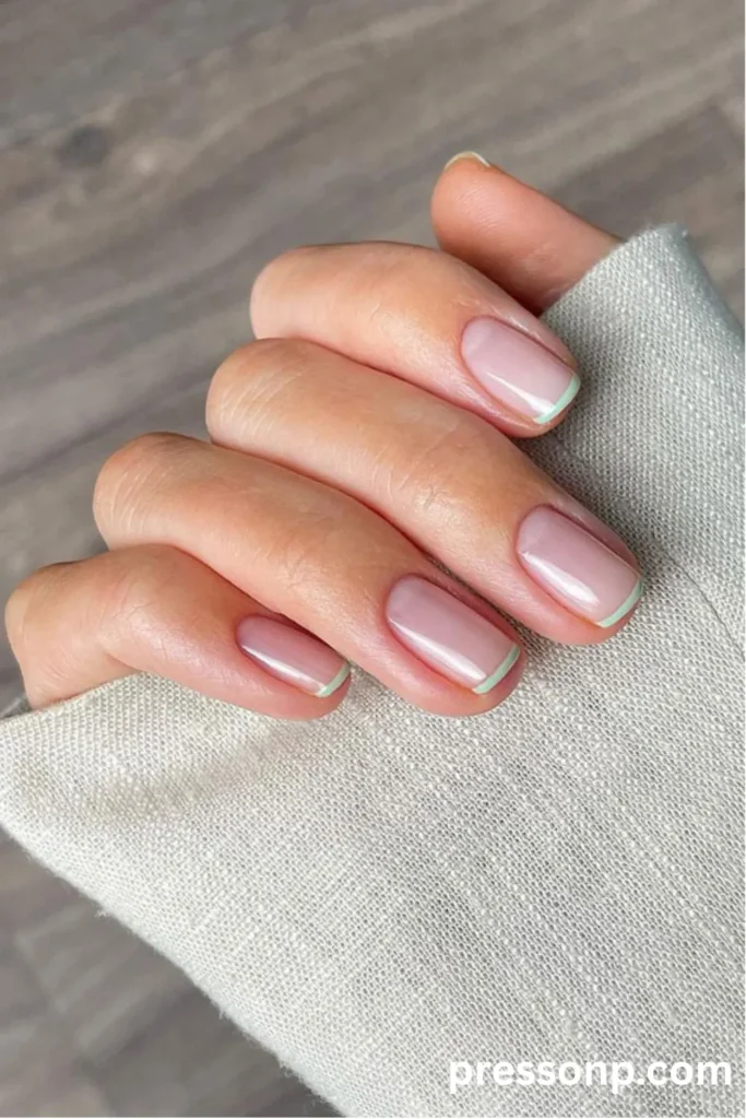 Close-up of short, square nails featuring a sheer nude base with ultra-thin, minimalist pastel mint green French tips.