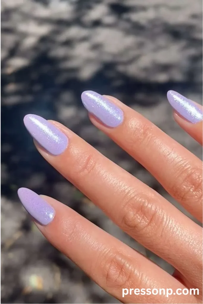 Close-up of long almond-shaped nails featuring a soft lavender polish topped with a shimmering, iridescent pearlescent chrome finish